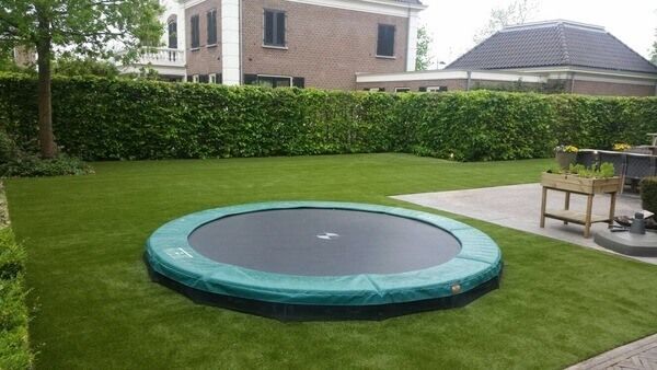 Tuin met trampoline in de grond en kunstgras erom heen