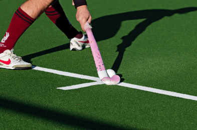 Man met roze hockey stick en bal op een kunstgrasveld