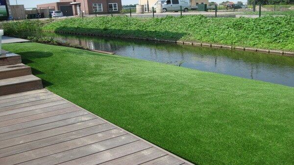 Tuin met vlonder en een trappetje met daarnaast kunstgras aan het water