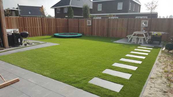 Tuin met een tegelpad naar een picknick tafel met daar om heen kunstgras en links in de hoek een trampoline