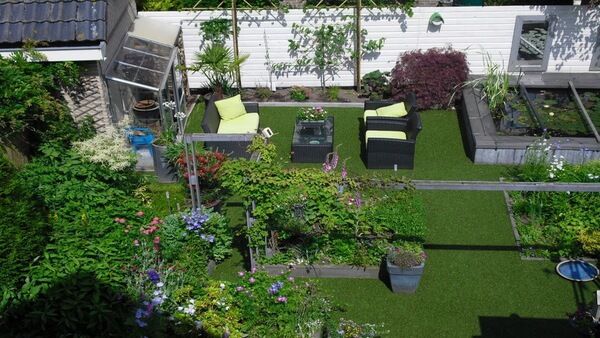 Bovenaanzicht van een tuin met kunstgras, een kas, planten en een lounge set