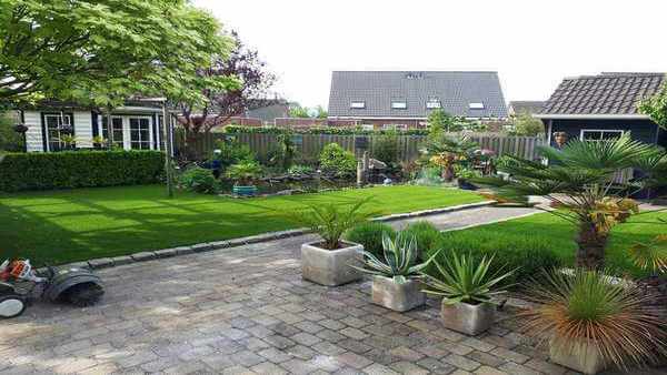 Tuin met tegels en plantenbakken en een stuk tuin met kunstgras