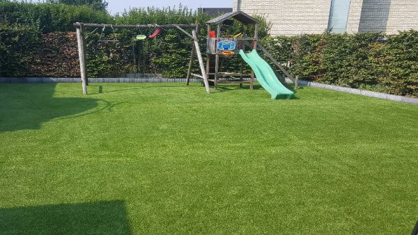 Tuin met kunstgras en een speeltuinhuisje met glijbaan en een schommel