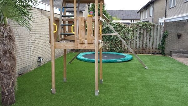 Tuin met kunstgras en een speelhuisje met schommel en daar achter een trampoline