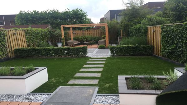 Tuin met kunstgras en plantenbakken met achteraan een houten overkapping met een lounge set