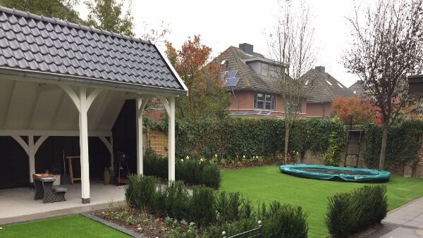Tuin met een witte overkapping, planten kunstgras en een trampoline