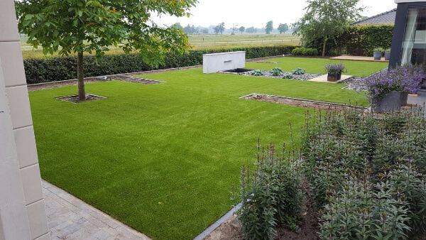 Tuin met kunstgras, planten en een boom